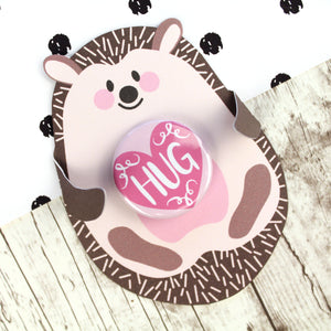 Cute pink and brown hedgehog with folded arms and a pink 'HUG' badge